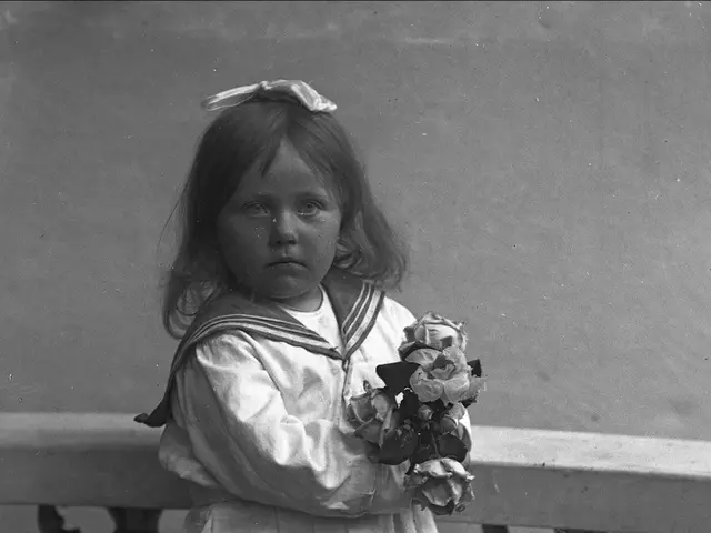 The image shows an old black and white photo of a little girl standing on a balcony, holding a...