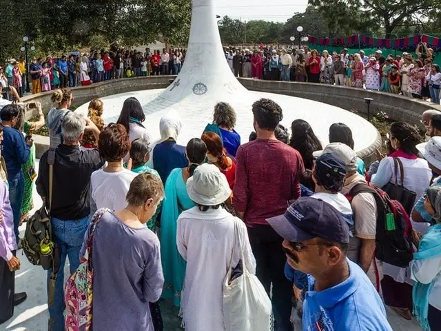 The image shows a large group of people standing in front of a white pillar, surrounded by light...