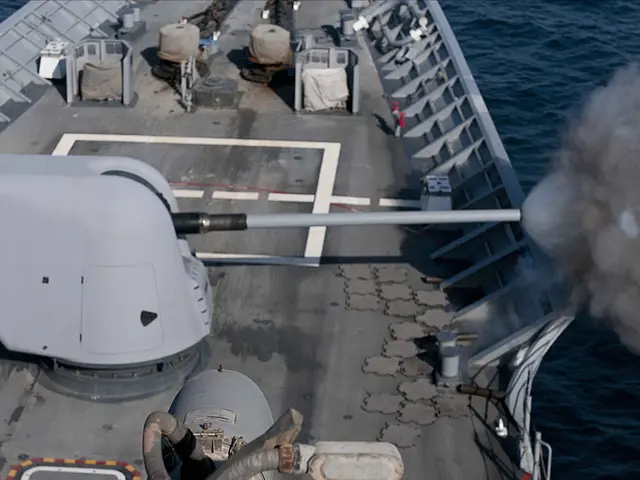 The image shows a navy ship in the ocean with smoke billowing out of its gun. On the deck of the...