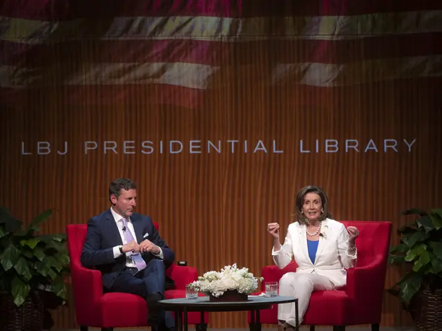 The image shows Nancy Pelosi and Chris Christie sitting on chairs in front of a table with a flower...