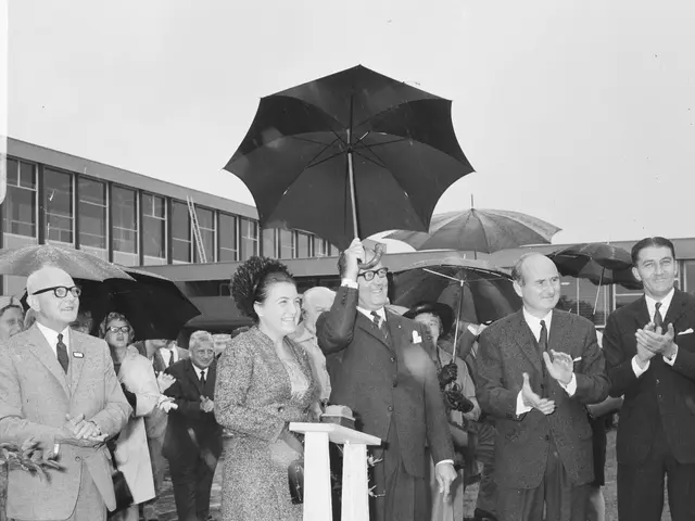 The image shows a group of people standing around a podium with an umbrella in the rain. The woman...