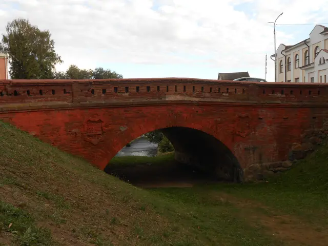 The image shows a red brick bridge spanning a river, with lush green grass on either side. In the...