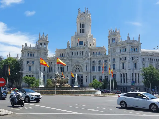 The image shows a bustling city street in Madrid, Spain, with vehicles on the road, a person riding...