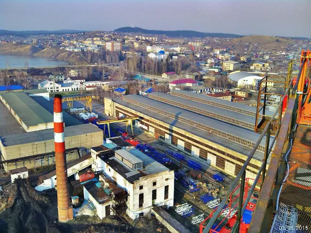The image shows an aerial view of a large factory with a crane in the foreground, surrounded by...