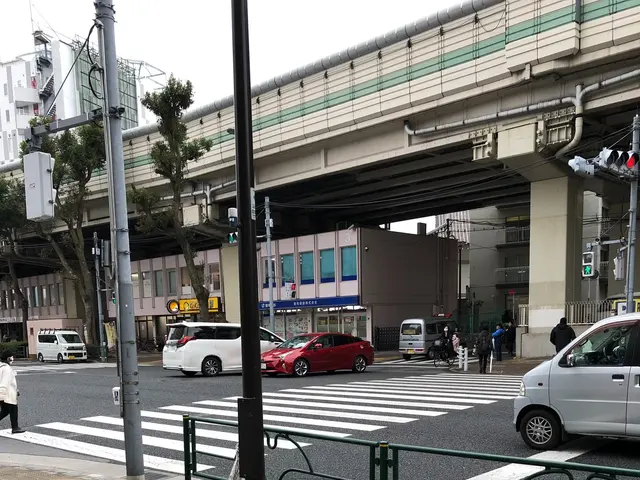 The image shows a city street with cars and people crossing the street at a crosswalk. There are...