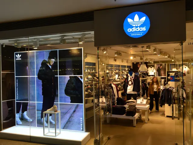 The image shows an adidas store in a shopping mall with mannequins in the window, clothes hung on...
