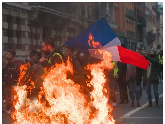 The image shows a group of people standing around a bonfire in the middle of a street, with a man...