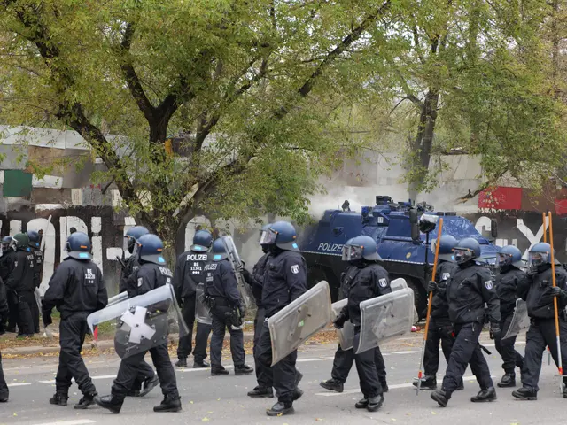 The image shows a group of police officers in riot gear walking down a street, wearing helmets and...