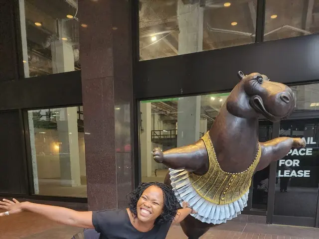 The image shows a woman in a mobility scooter with her arms outstretched in front of a statue of a...