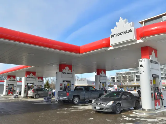 The image shows a petrol station with cars parked in front of it, surrounded by buildings, trees,...