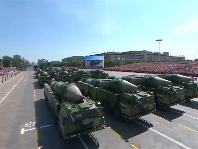 The image shows a military parade in Pyongyang, North Korea, with military vehicles on the road and...