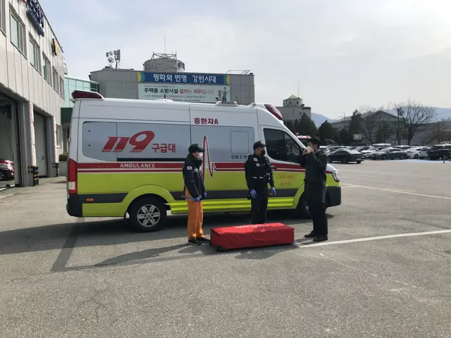 The image shows an ambulance parked in a parking lot next to a building, with three people standing...