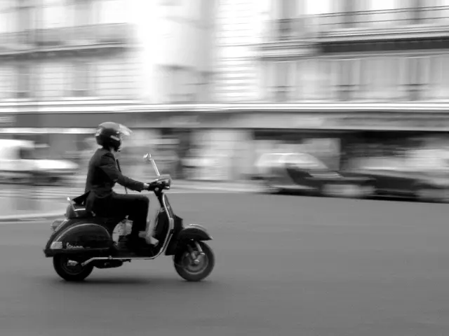 In this image i can see a person riding scooter on the road.
