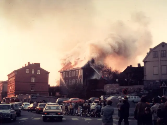 The image shows a large fire burning in the middle of a street, with smoke billowing up into the...