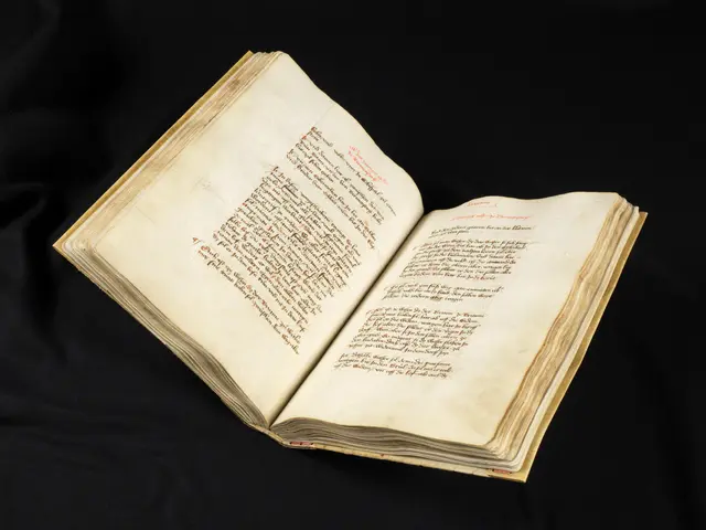 The image shows an open book with red writing on it, set against a black background. The book...