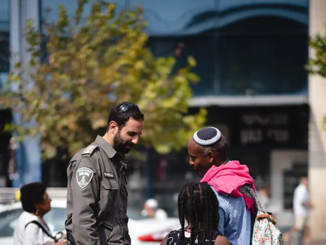 The image shows a police officer talking to a group of people on the street. There is a stroller in...