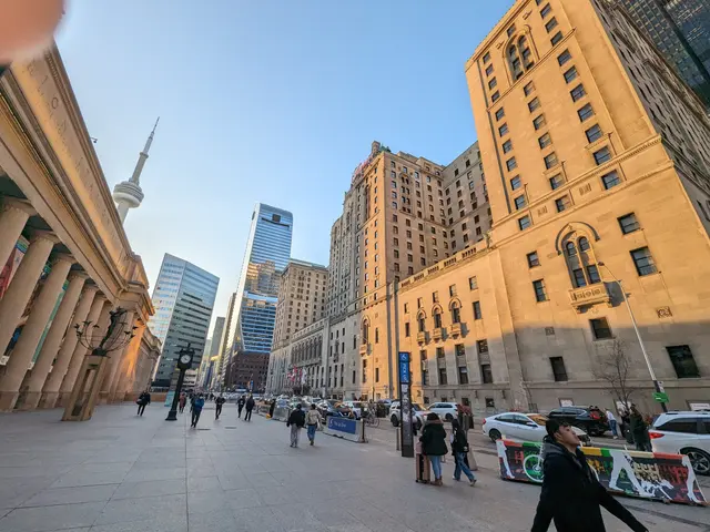 The image shows a bustling city street in Toronto, Ontario, Canada, with tall buildings in the...