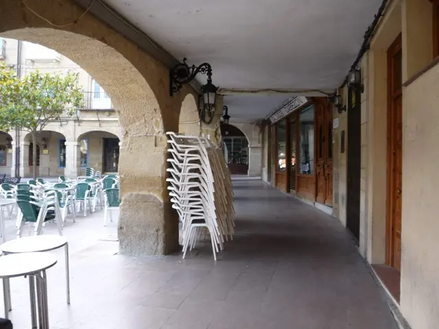 The image shows a building with windows and doors, a group of chairs and tables sitting on the side...