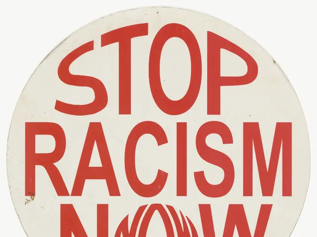 The image shows a white background with a sign that reads "Stop Racism Now" in bold black...