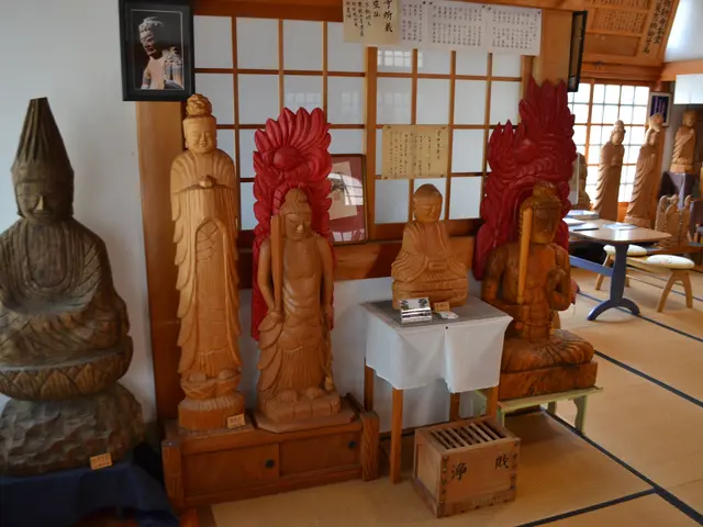 The image shows a room filled with lots of wooden Buddha statues on the floor, a table with a cloth...