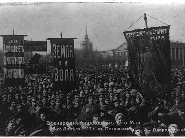 The image shows a large crowd of people standing in front of a building, holding banners with text...