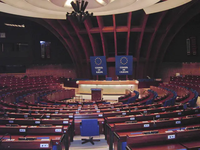 The image shows the European Parliament in Brussels, Belgium. It is a large room with tables and...