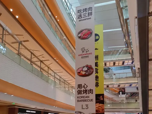 The image shows an inside view of a shopping mall with an escalator in the middle. There are people...