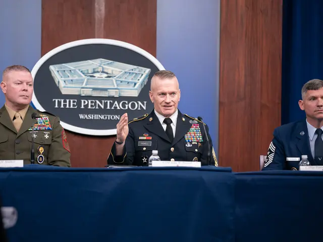 The image shows three men in military uniforms sitting at a table with a blue cloth draped over it....