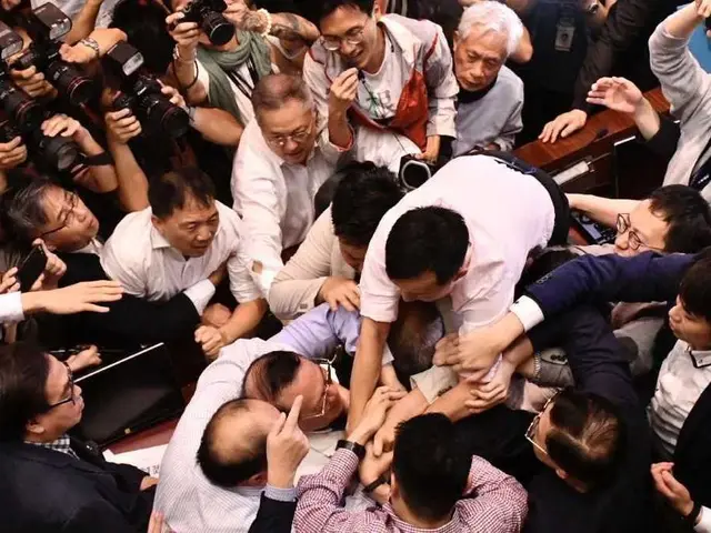 The image shows a group of people standing around each other in front of a crowd, some of them...