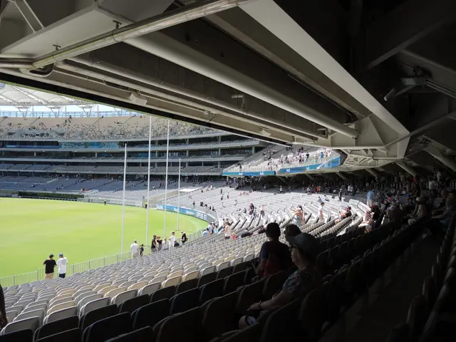 The image shows a large stadium filled with lots of people watching a game. There are people...