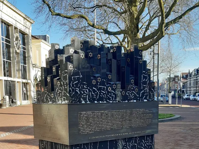 The image shows a memorial in the middle of a city square with a tree in front of it. On the ground...
