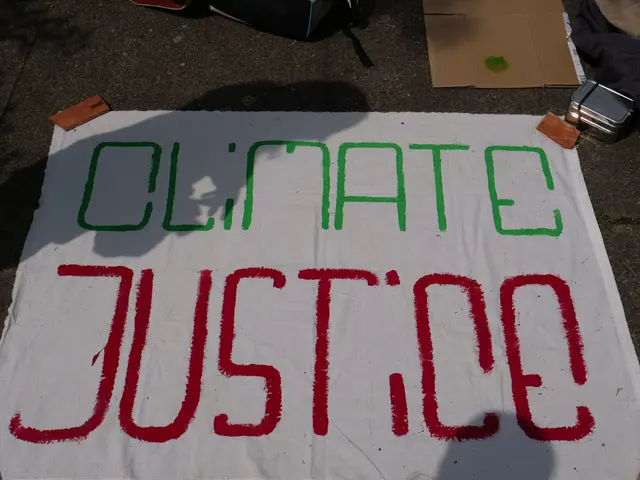 The image shows a white banner with the words "climate justice" written on it, placed on the ground...