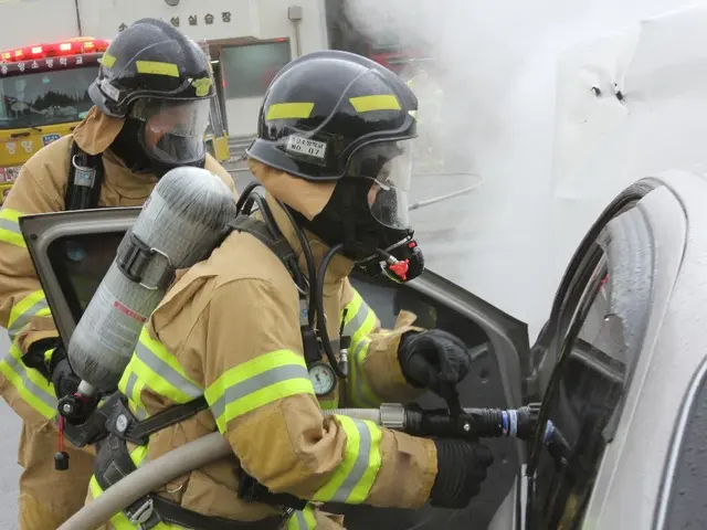 The image shows two firefighters in protective gear, wearing helmets and gloves, using a hose to...