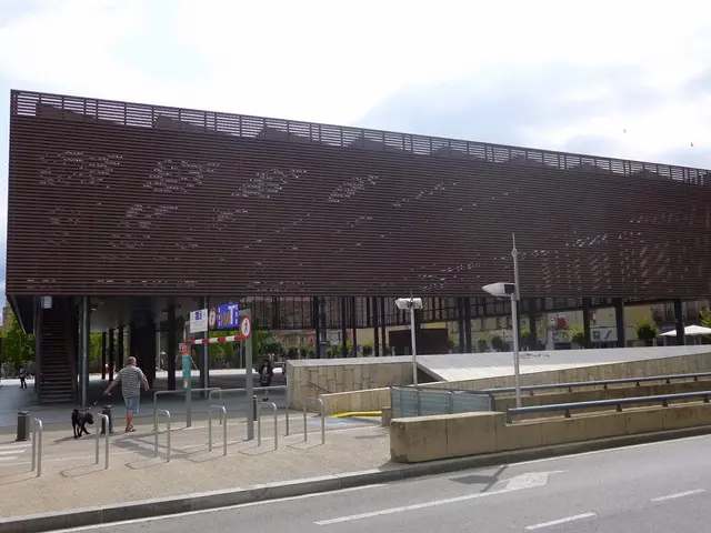 The image shows a large building with a lot of windows on the side of it, surrounded by street...