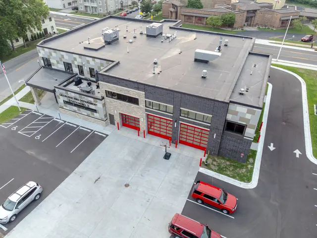 The image shows an aerial view of a fire station with cars parked in front of it, surrounded by...