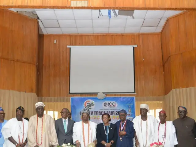 The image shows a group of people standing around a table covered with a white cloth, adorned with...