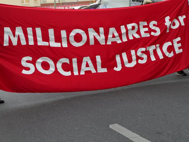 The image shows a group of people walking down a street, holding a red banner that reads...