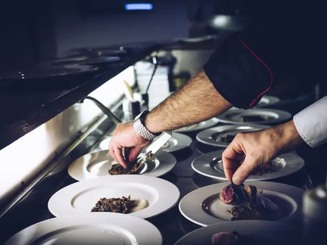 The image shows a chef in a kitchen, wearing a watch and holding a knife and fork in his hands. On...