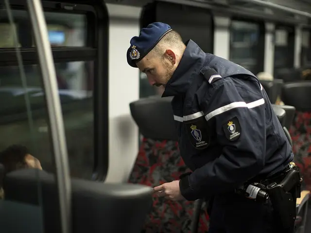 The image shows a police officer standing on a train, looking at his cell phone. He is wearing a...
