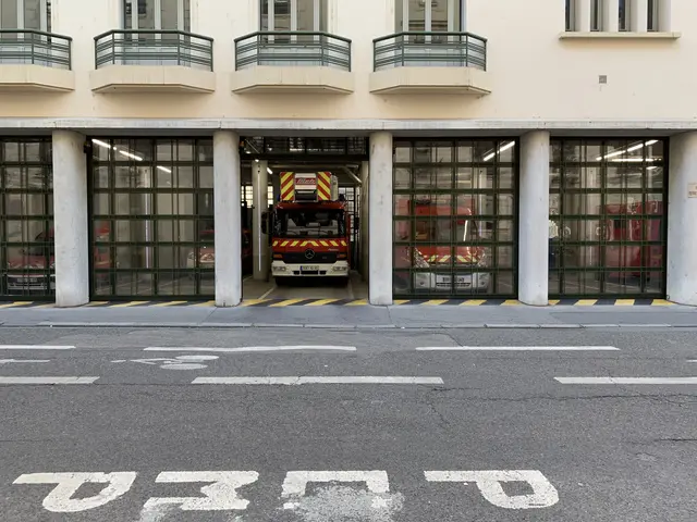 The image shows a fire station with a fire truck parked in front of it. The building has windows,...
