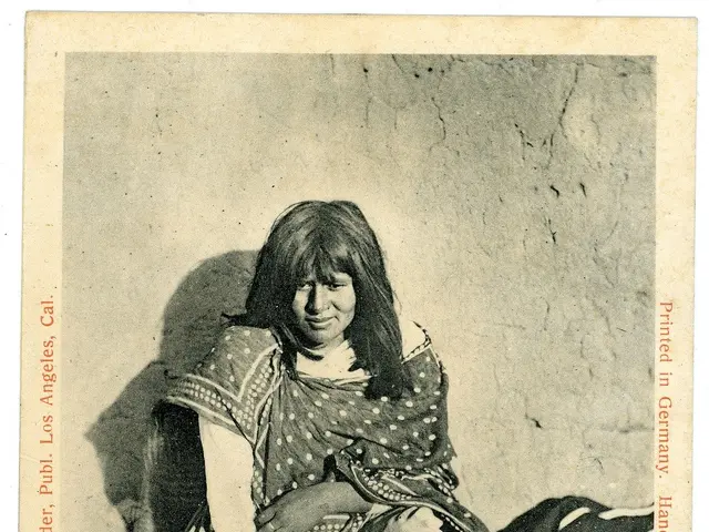 The image shows an old photo of a Native American woman sitting on the ground with a pot in front...