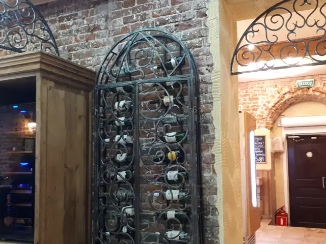 The image shows a wine cellar with a brick wall and a metal gate. Inside the cellar, there are...
