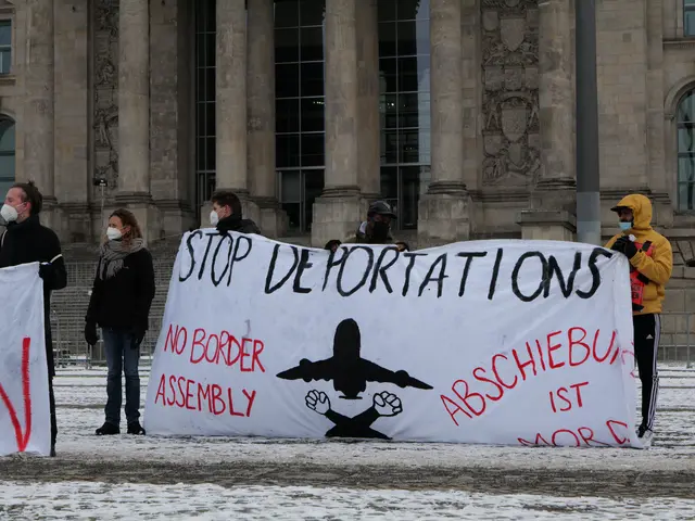 The image shows a group of people standing in front of a building, holding a banner that reads...