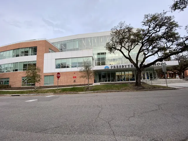 The image shows a large building with a lot of windows on the side of it, surrounded by trees,...