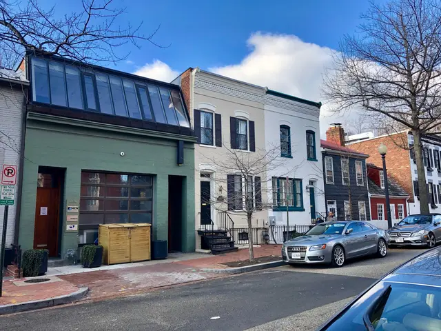 The image shows a street with cars parked on the side of it, surrounded by buildings with windows,...