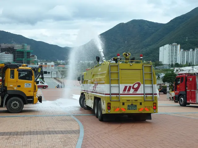 The image shows a group of fire trucks parked next to each other in a parking lot surrounded by...