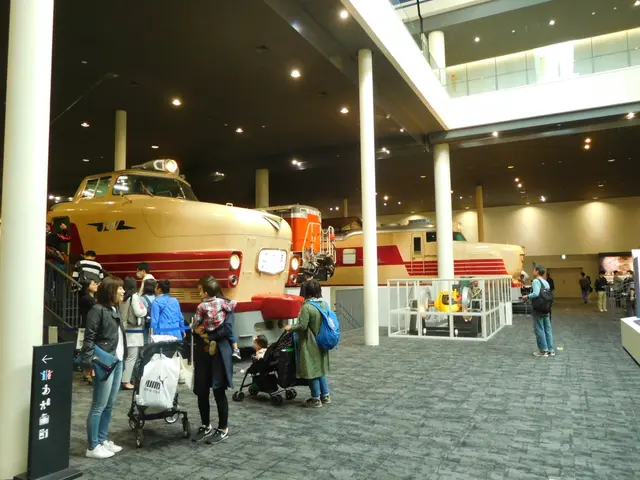 The image shows a group of people standing in front of a train in a museum. Some of the people are...