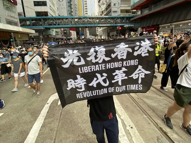 The image shows a group of people walking down a street in Hong Kong, holding a banner that reads...