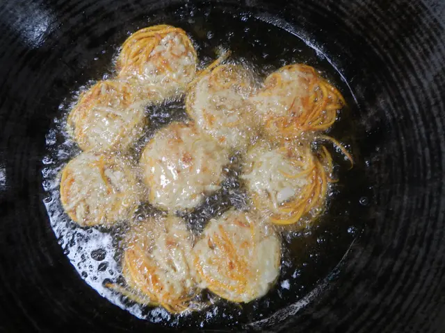 The image shows a frying pan filled with fried food on top of a stove. The food is sizzling in the...