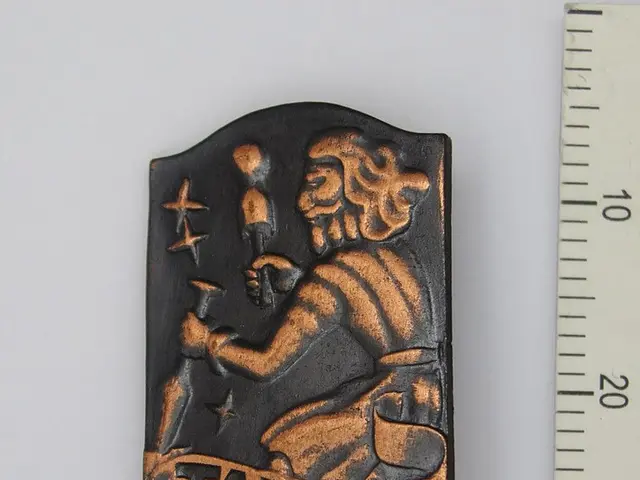 The image shows a small metal plaque with the word "Tallinn" on it, placed on a white surface with...